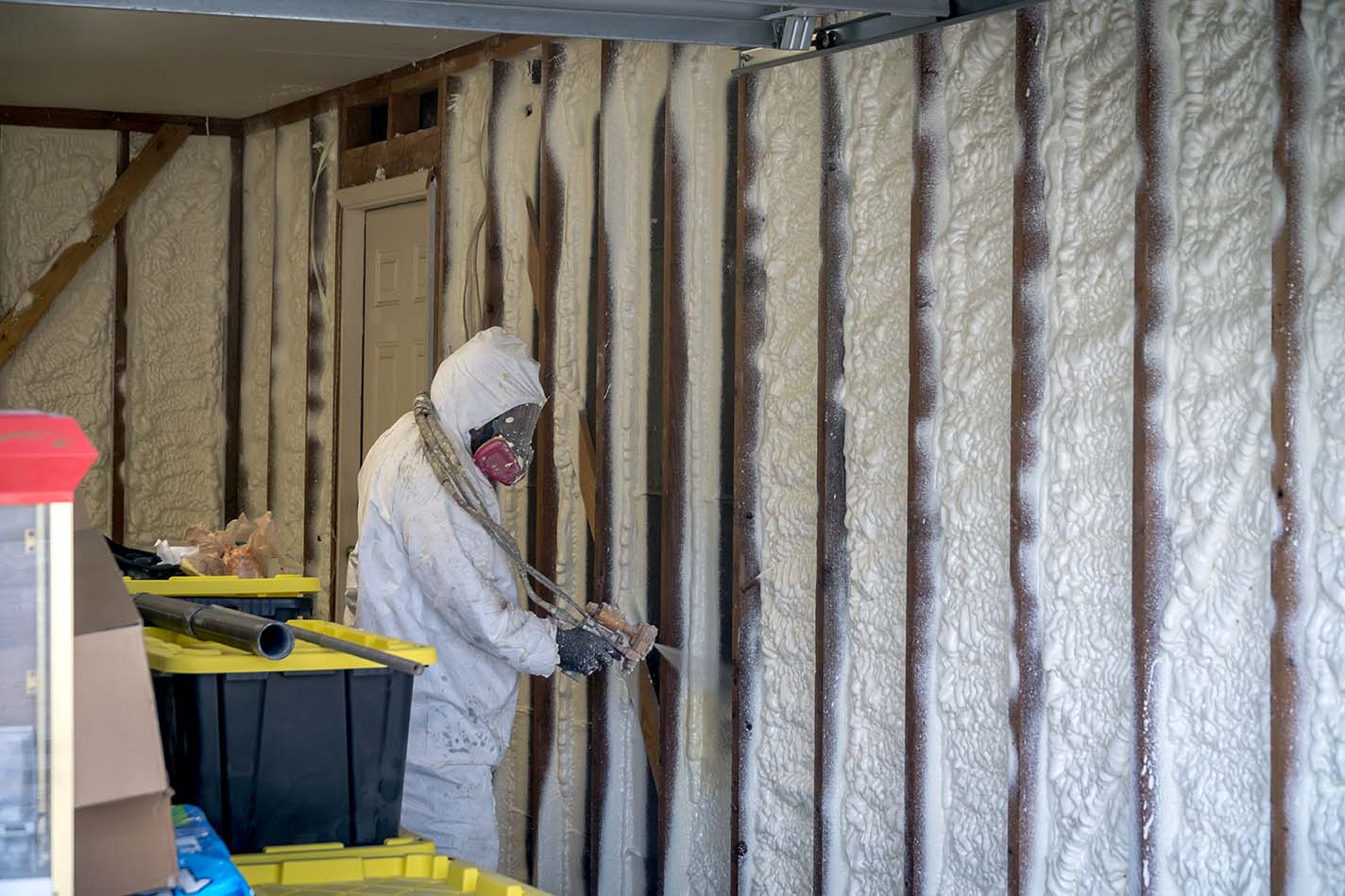 Spray Foam Insulation Services 2 Installer spraying closed-cell foam into open garage wall stud bays, foam expanding flush to the studs
