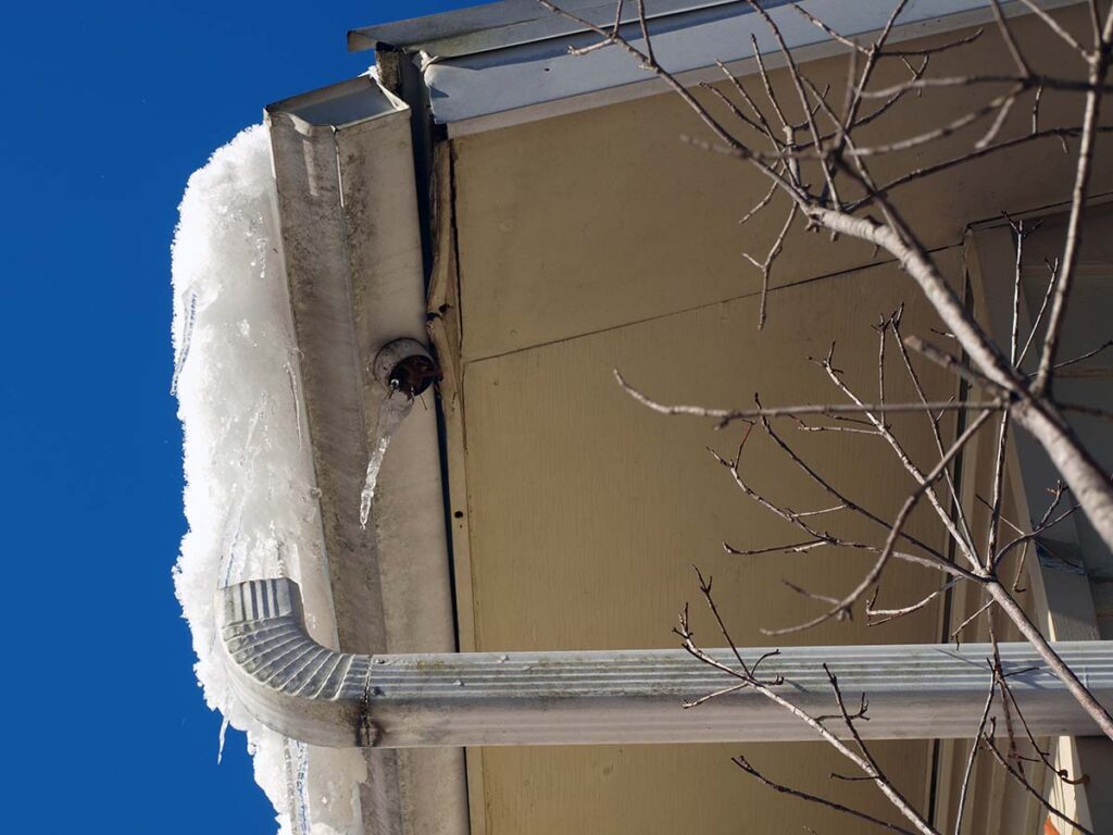 Ice dam on roof causing damage to gutters due to poor insulation in attic.